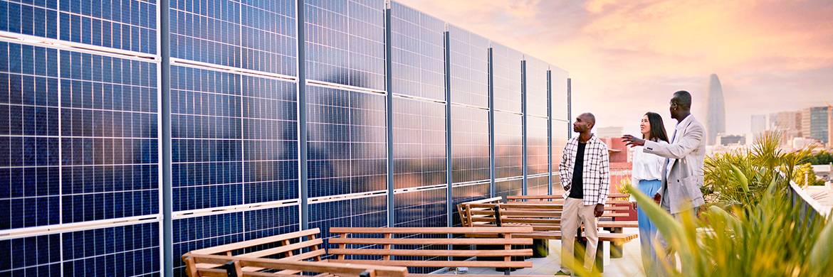 Three people look at solar panels on the terrace of an office building