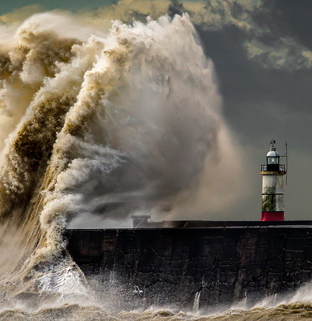 A wave about to hit a lighthouse in a storm