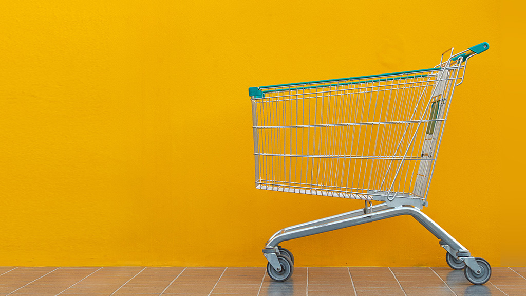 An empty shopping cart sits outside a store in front of a yellow wall