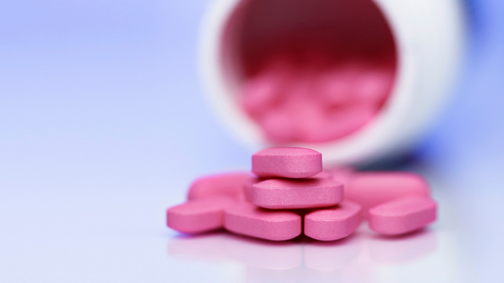 Pink tablets sit in front of an overturned pill bottle